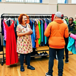 A vibrant clothing swap event in a community hall, featuring diverse individuals exchanging pre-loved clothes, showcasing the fun and sustainable way to refresh wardrobes. Capture the lively atmosphere and community spirit.